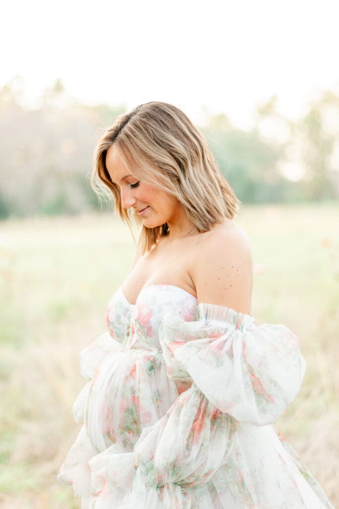 mom with short blonde hair holding her baby bump in a long flowy maternity gown.