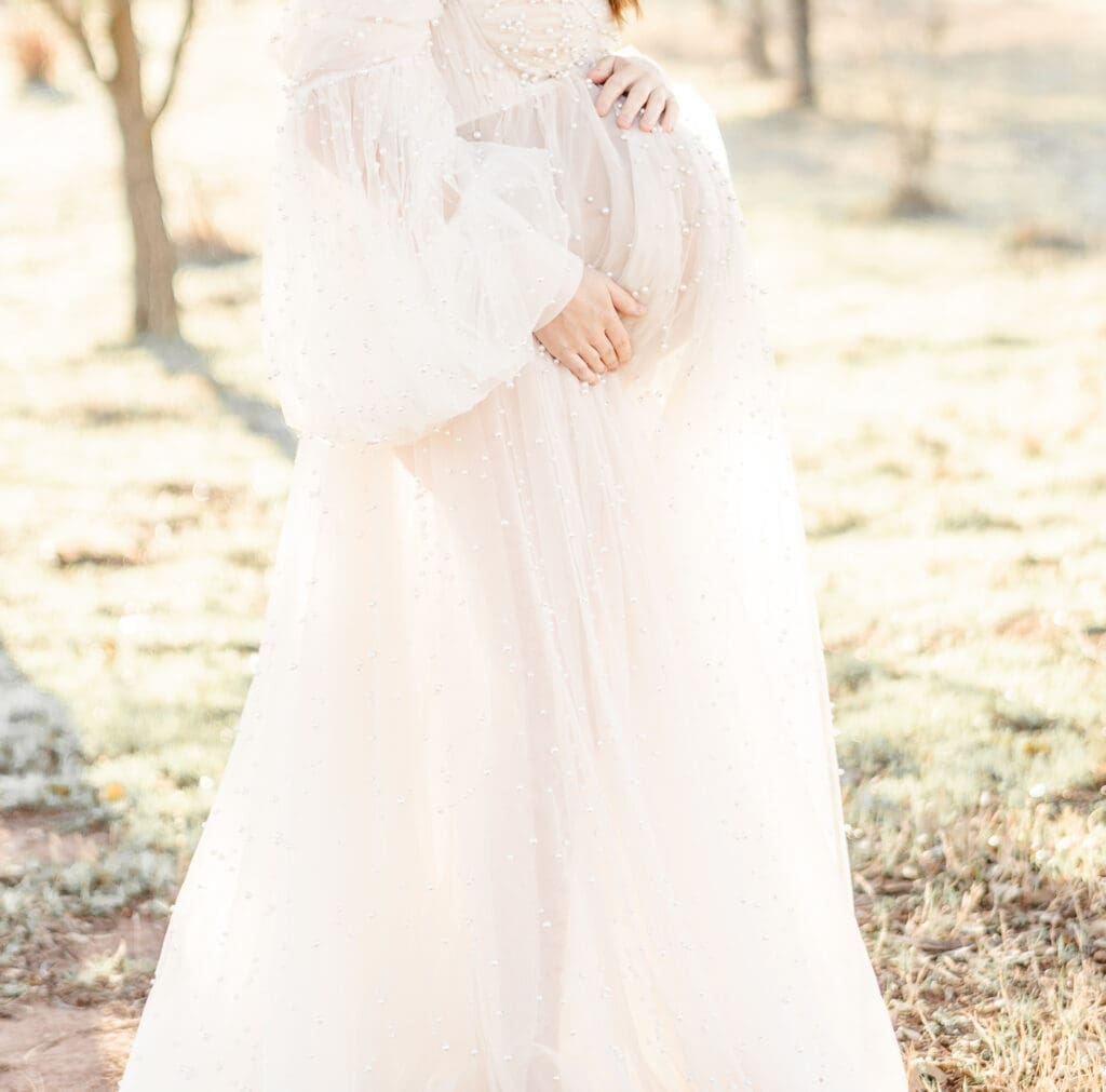 An off white maternity gown with long puff sleeves that features pearls throughout the gown. Designed by KH Fashions.