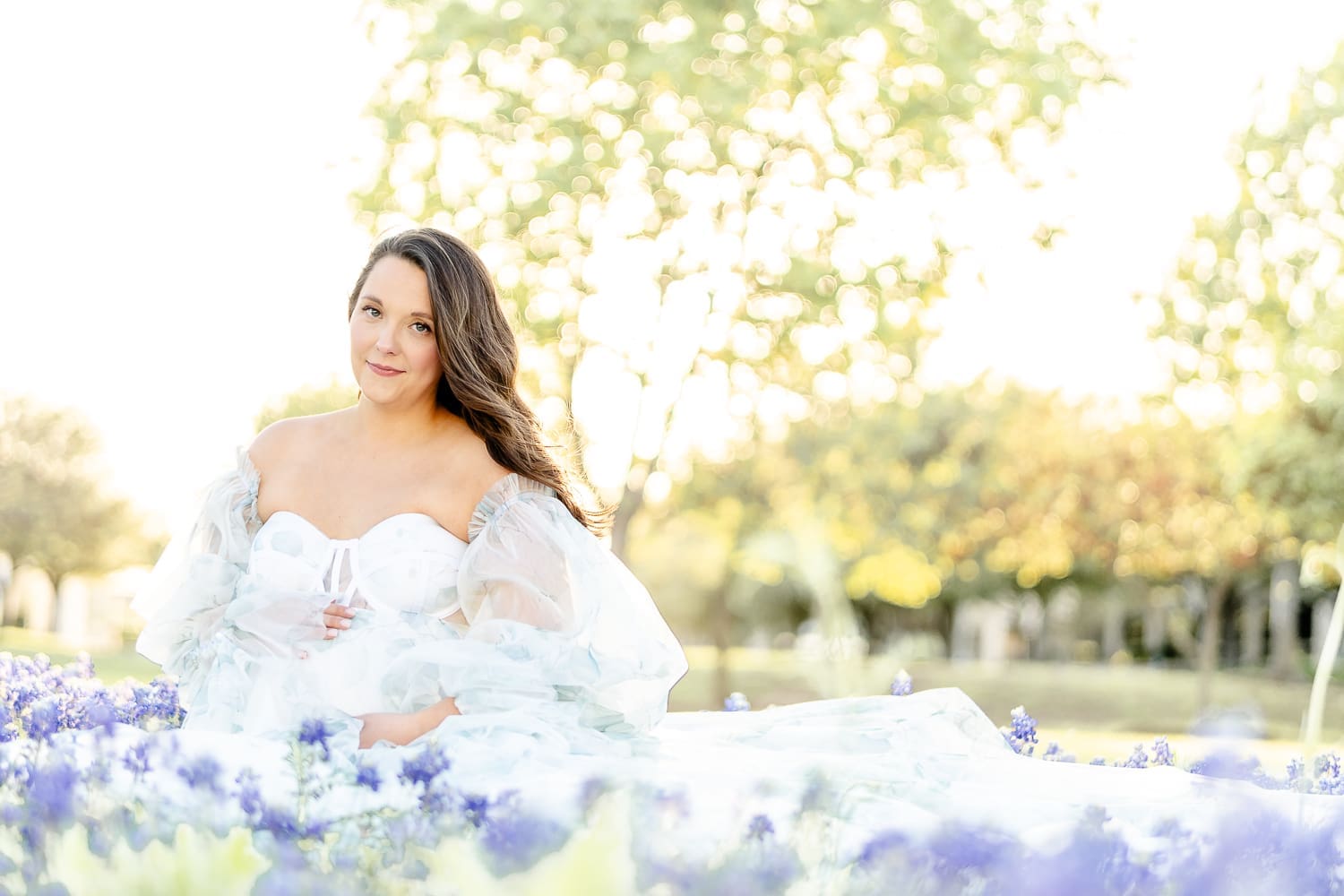 maternity session with a mom wearing a maternity gown while sitting in a field of bluebonnets