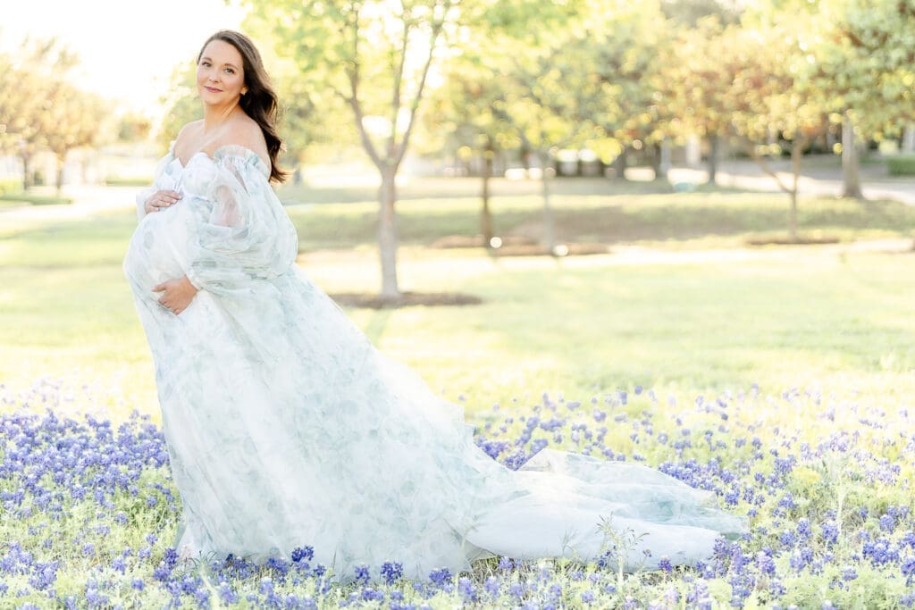 A long white maternity gown with overlays of oft sage green leaves, featuring removable puff sleeves. Designed by KH Fashions.